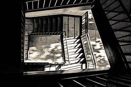 Academic Interventions: Responsibilities of Scholarship in Polycrisis Conditions Abstract birds-eye-view of institutional staircase.